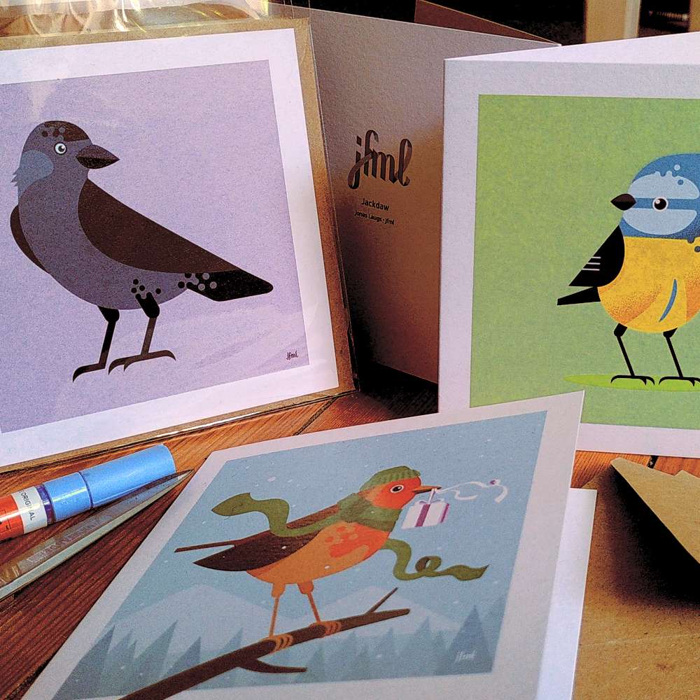 Photo of three square greeting cards with birds on them, on a wooden floor.